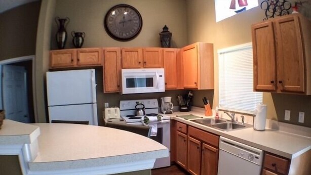 A compact kitchen with wooden cabinets, a microwave, a refrigerator, and a sink. - Perfect For Your Florida Vacation! 3 Bedroom Home by RedAwning (Haines City)