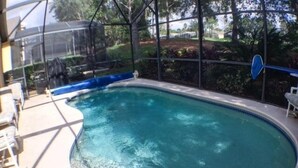 A swimming pool with a clear blue water surface, surrounded by a covered area with chairs and a view of the outdoors. - Perfect For Your Florida Vacation! 3 Bedroom Home by RedAwning (Haines City)