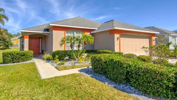 Une maison de plain-pied avec une porte rouge, une façade de couleur beige et un garage.