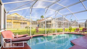 Un espace piscine doté d’une enceinte en verre, de chaises longues et offrant une vue sur les maisons au loin.