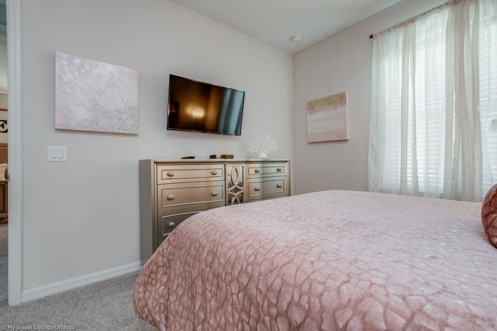 A bedroom with a bed, a TV mounted on the wall, and a dresser.
