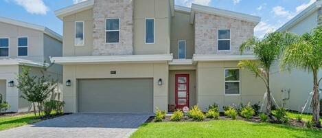 A modern two-story house with a red door, a garage, and a well-maintained lawn.
