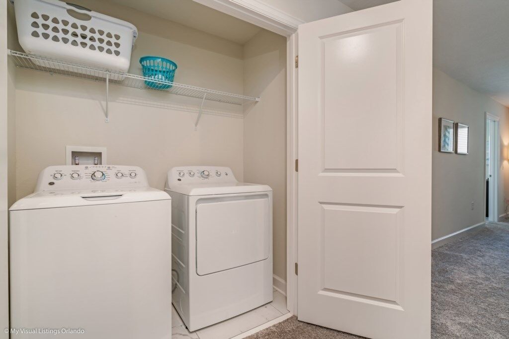 A laundry room with two white front-loading washers and dryers, a white door, and a shelf with laundry baskets.