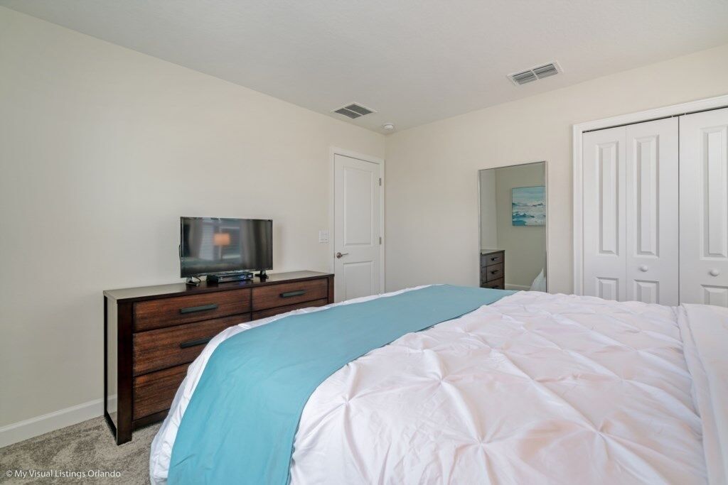 A bedroom with a bed, a dresser, a television, and a closet.