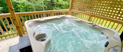 A hot tub on a wooden deck with a view of a forest.