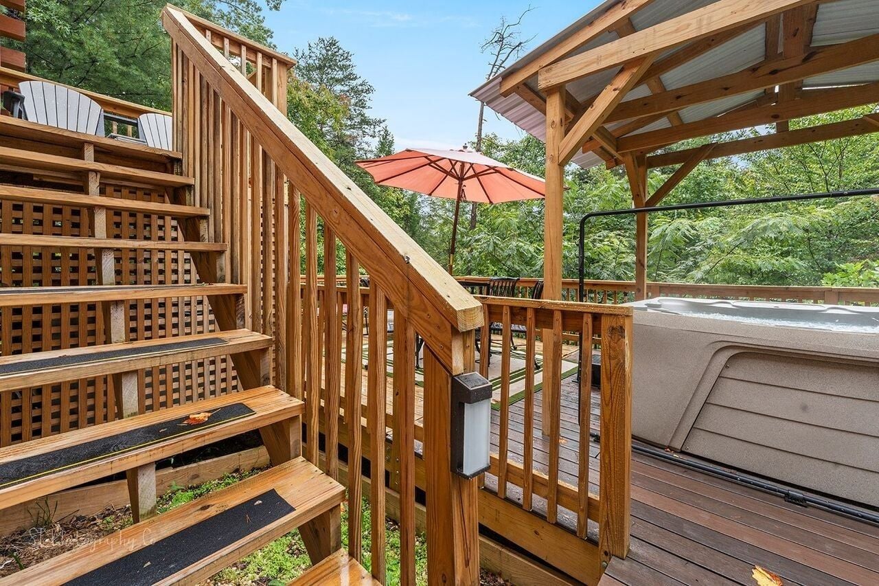 A wooden deck with a hot tub, a wooden staircase, and a covered seating area.