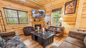 A cozy cabin interior with wooden walls, a fireplace, a television, and a bookshelf. - Foxes' Den Cabin with Private Hot Tub and Arcade Game by RedAwning (Pigeon Forge)