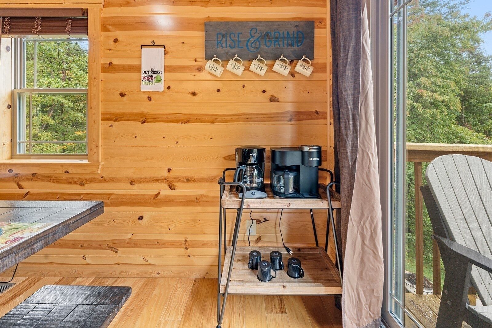 A cozy cabin interior with wooden walls, a coffee station, and a sign that reads "RISE & GRIND".