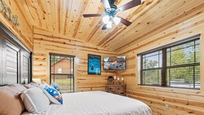 A wooden cabin bedroom with a bed, a ceiling fan, a dresser, and a TV mounted on the wall. - Foxes' Den Cabin with Private Hot Tub and Arcade Game by RedAwning (Pigeon Forge)