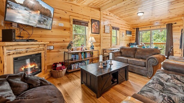 A cozy cabin interior with a fireplace, wooden walls, a television, and a comfortable seating area. - Foxes' Den Cabin with Private Hot Tub and Arcade Game by RedAwning (Pigeon Forge)