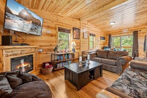 A cozy cabin interior with a fireplace, wooden walls, a television, and a comfortable seating area. - Foxes' Den Cabin with Private Hot Tub and Arcade Game by RedAwning (Pigeon Forge)