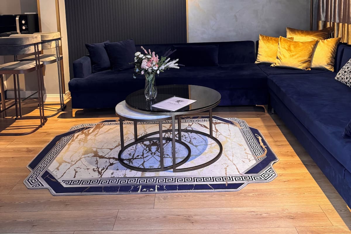 A modern living room with a dark blue sofa, a round coffee table with a vase of flowers, and a patterned rug.