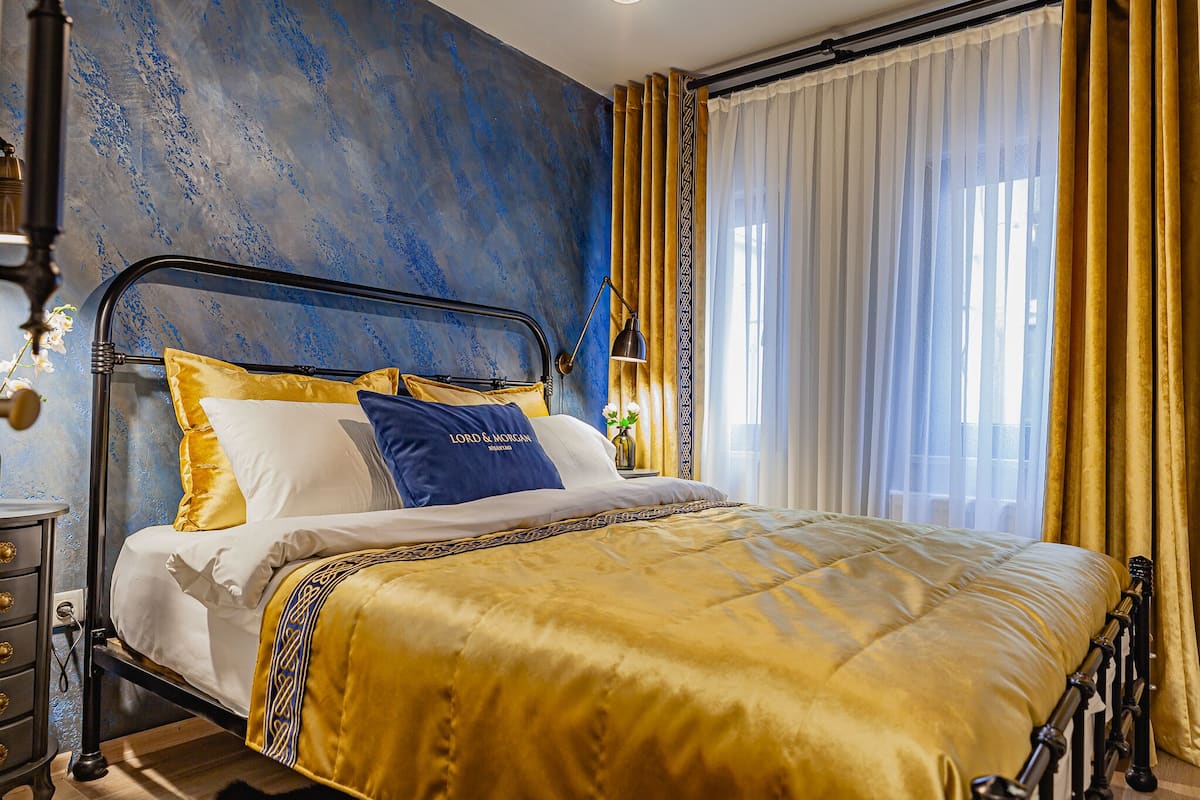 A bed with a gold and blue bedspread, a metal frame, and a nightstand with a lamp.