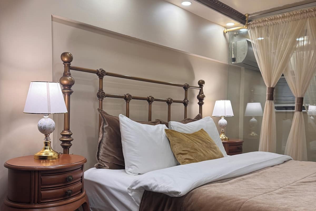 A neatly made bed with a wooden headboard, two bedside tables with lamps, and a window with sheer curtains.
