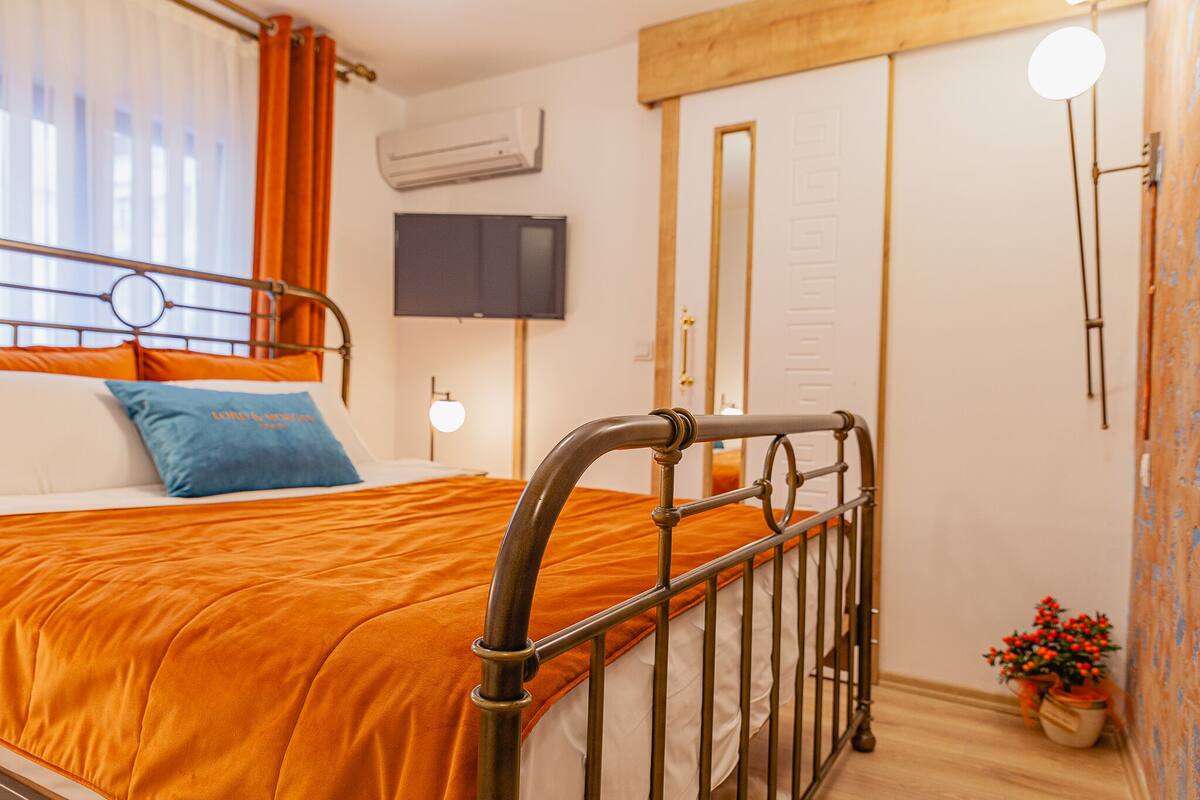 A bedroom with a metal bed frame, a television mounted on the wall, and a potted plant by the window.