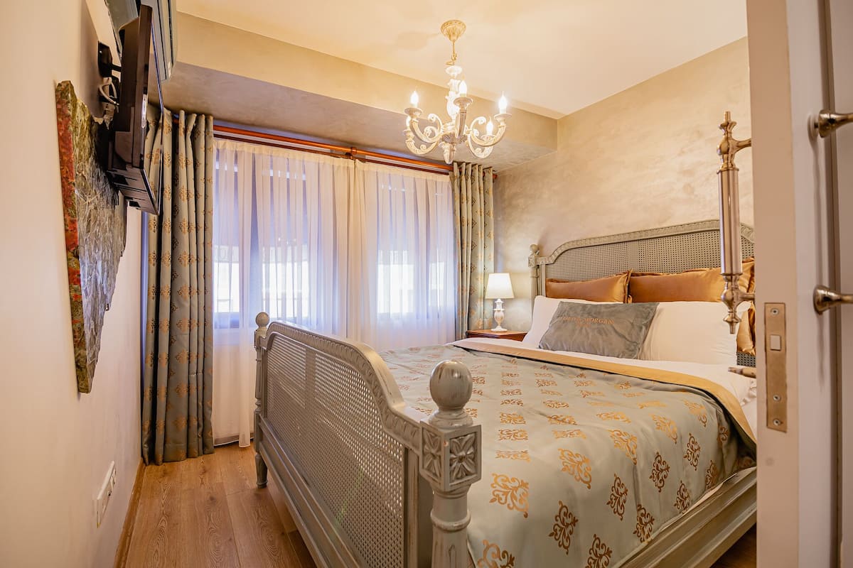 A bedroom with a bed, curtains, a chandelier, and a nightstand.