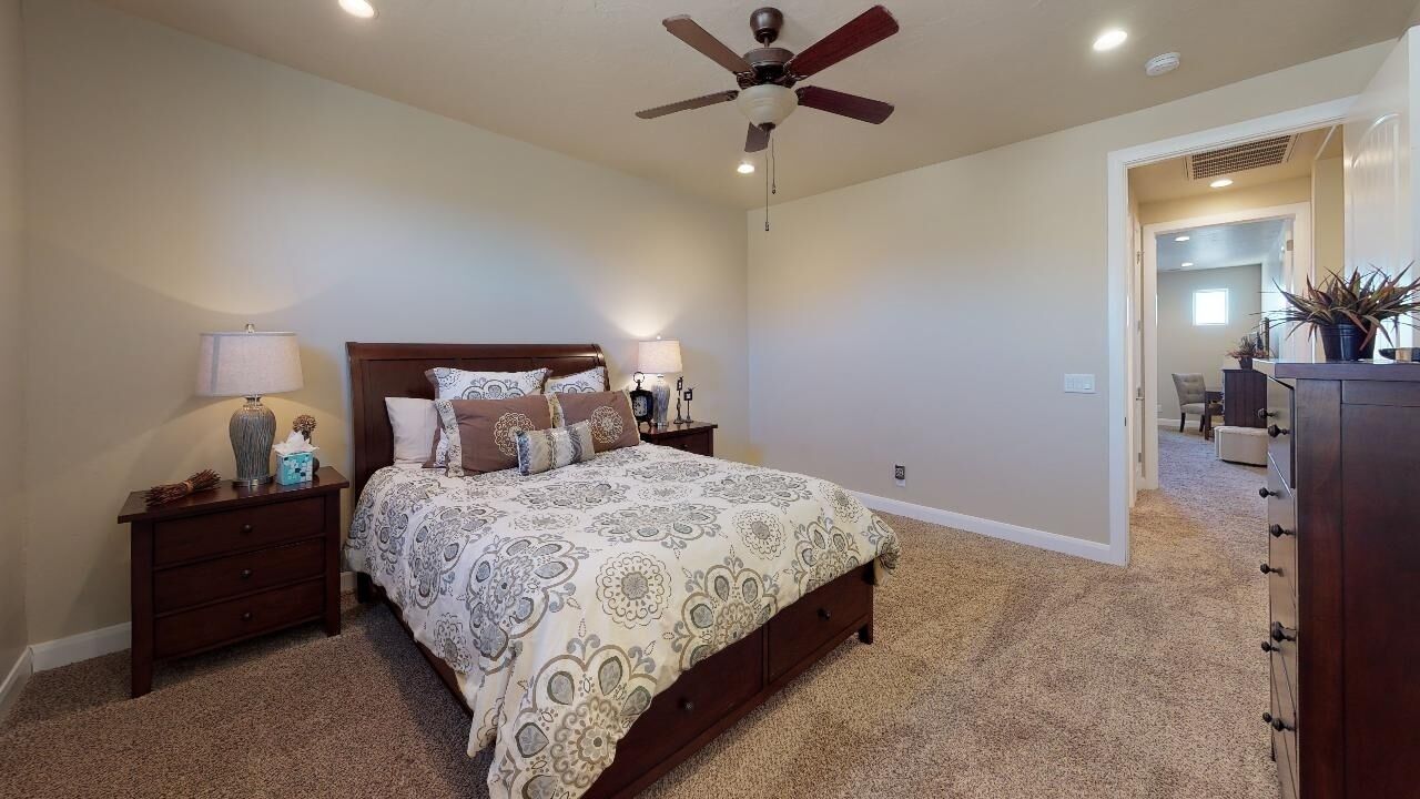 A bedroom with a large bed, two bedside tables, a ceiling fan, and a carpeted floor.