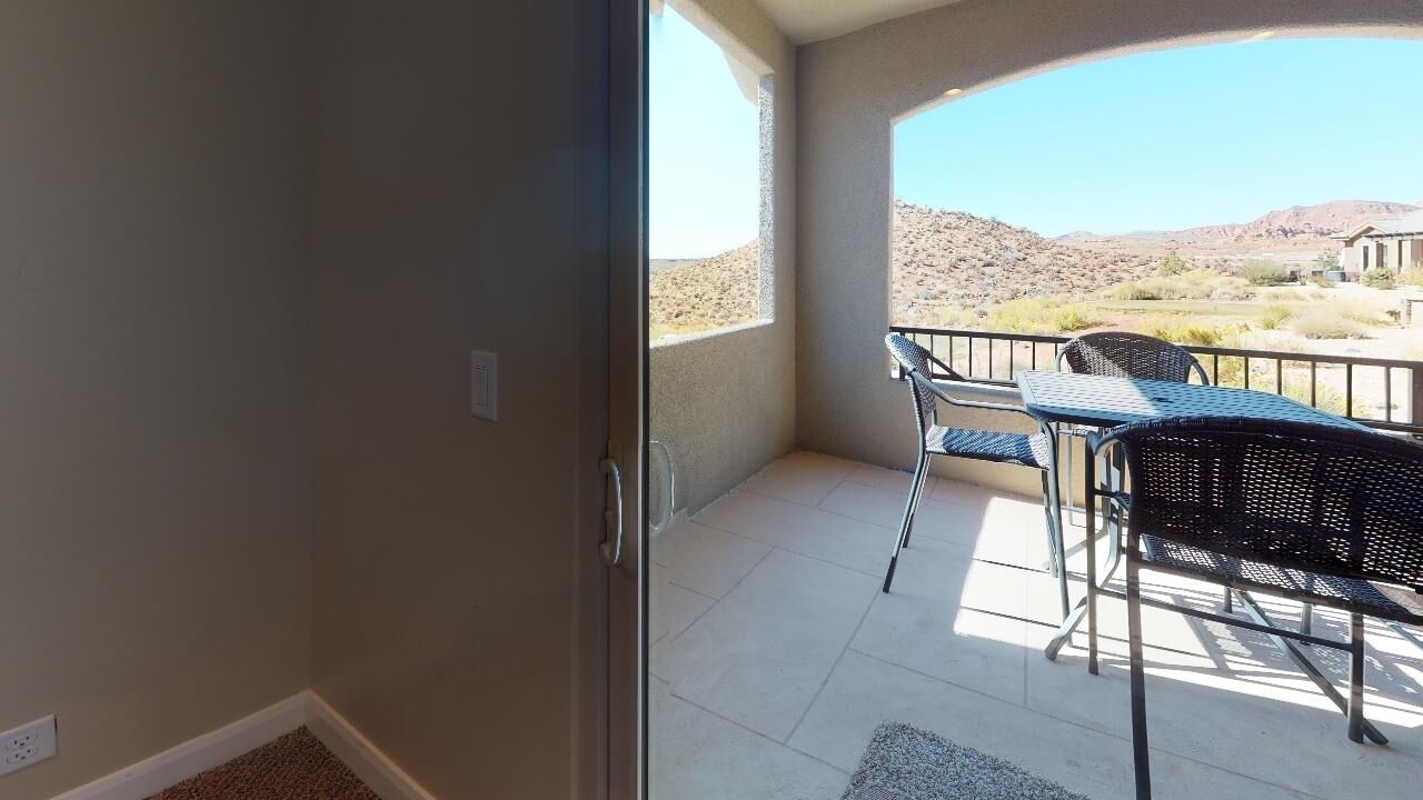 A balcony with a view of a desert landscape, a table with chairs, and a door leading to the interior.