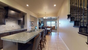 A kitchen with granite countertops, dark wooden cabinets, and a central island with bar stools.