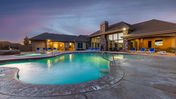 A swimming pool with lounge chairs, a stone facade, and a sunset sky.