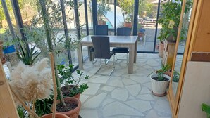 Un espace patio avec une table et des chaises, entouré de plantes en pot et doté d’un sol en pierre.