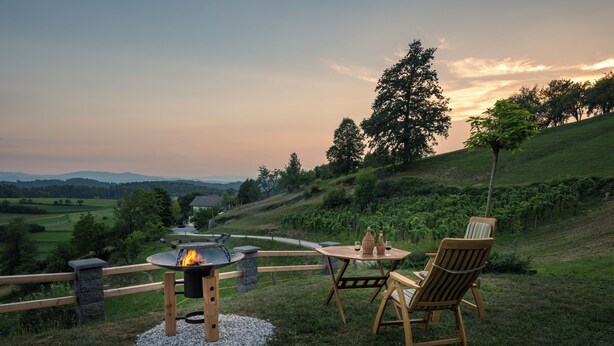 Een terras met een vuurkuil, houten stoelen en een tafel.