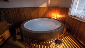 Een kamer met houten vloer, een groot rond bubbelbad, een champagnefles en een glas op de vloer.