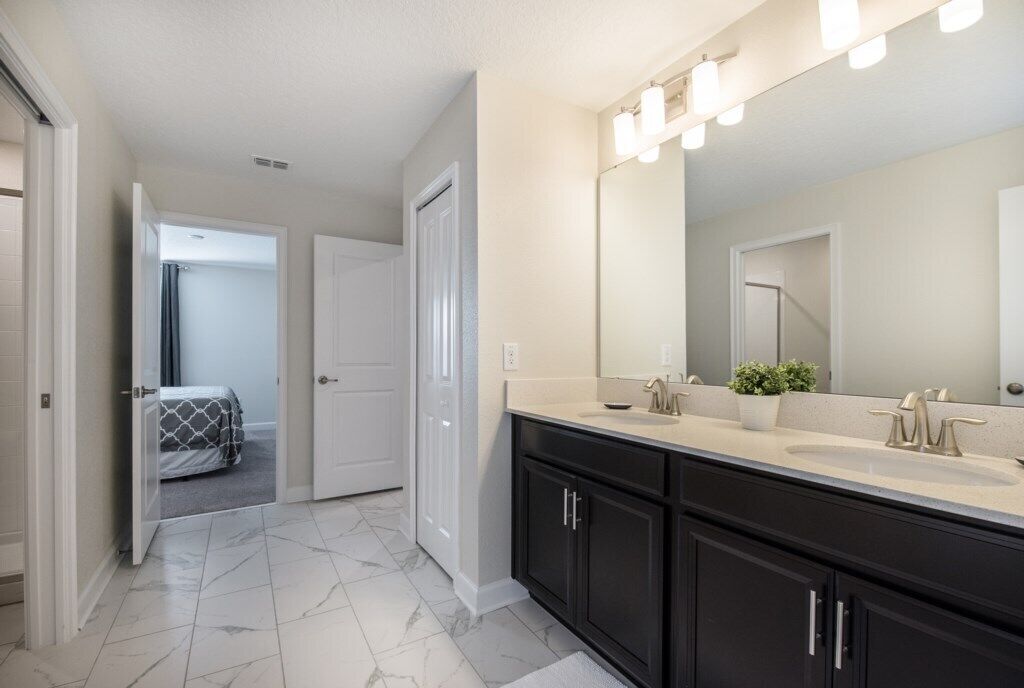 A modern bathroom with a large mirror, dual sinks, and a walk-in shower.