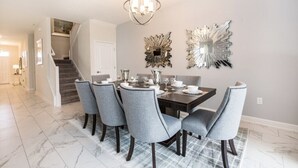 Uma área de refeições com uma mesa de madeira escura, seis cadeiras estofadas cinzas e dois espelhos decorativos na parede.