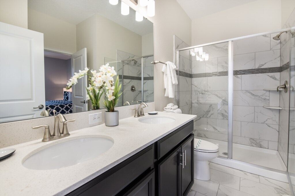 A modern bathroom with two sinks, a shower, and a toilet.