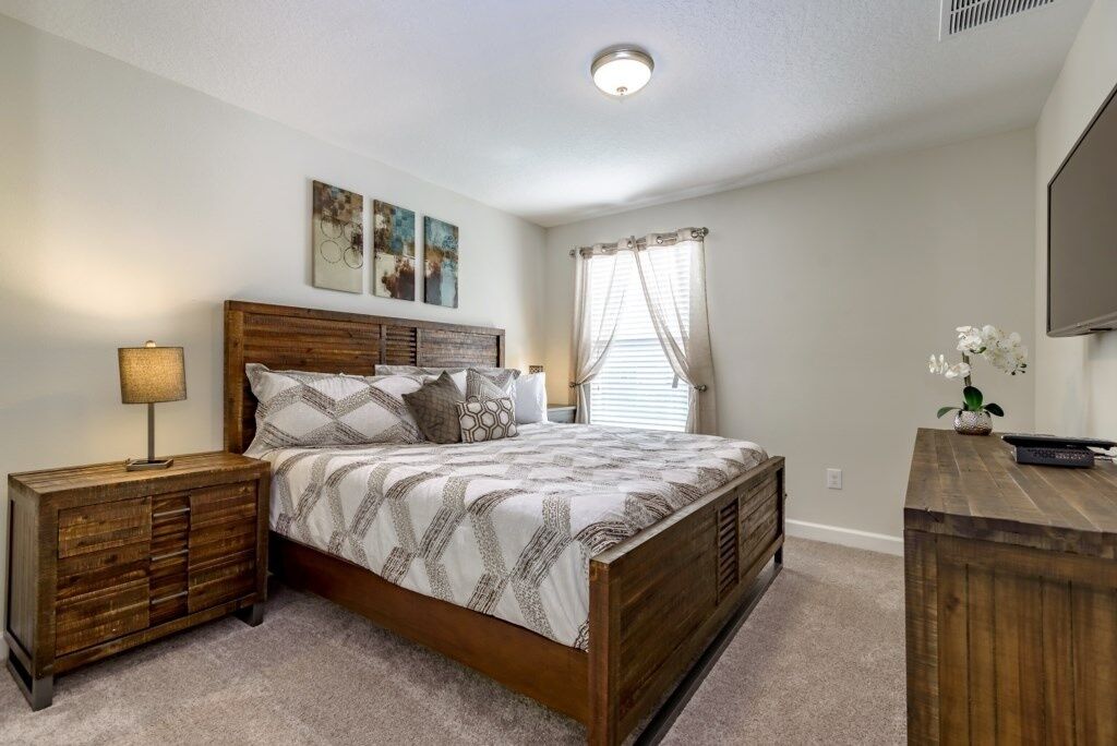 A bedroom with a wooden bed, a nightstand, a dresser, and a TV on a wooden stand.