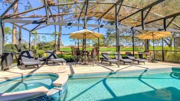 Una piscina exterior techada con sillas de descanso y sombrillas, rodeada por una estructura metálica y árboles.