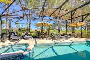 A covered outdoor swimming pool with lounge chairs and umbrellas, surrounded by a metal frame and trees.