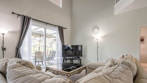 Una sala de estar con un sofá, un televisor sobre un mueble bajo y una mesa de centro de vidrio.