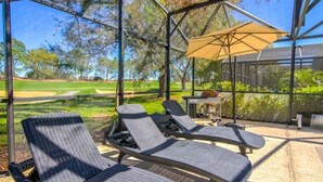 Un espacio al aire libre techado con sillones de descanso y una mesa, con vista a un campo de golf.