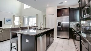 A modern kitchen with a central island, stainless steel appliances, and dark cabinetry. - 1585tempo 5 Bedroom Home by RedAwning (Davenport)