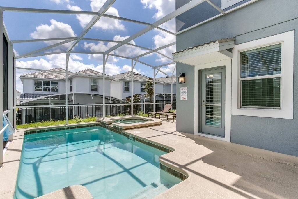A pool area with a covered patio, adjacent buildings, and a clear sky.