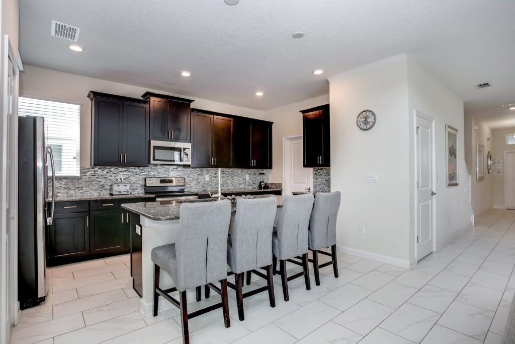 A modern kitchen with dark cabinets, a granite countertop, and a central island with bar stools.