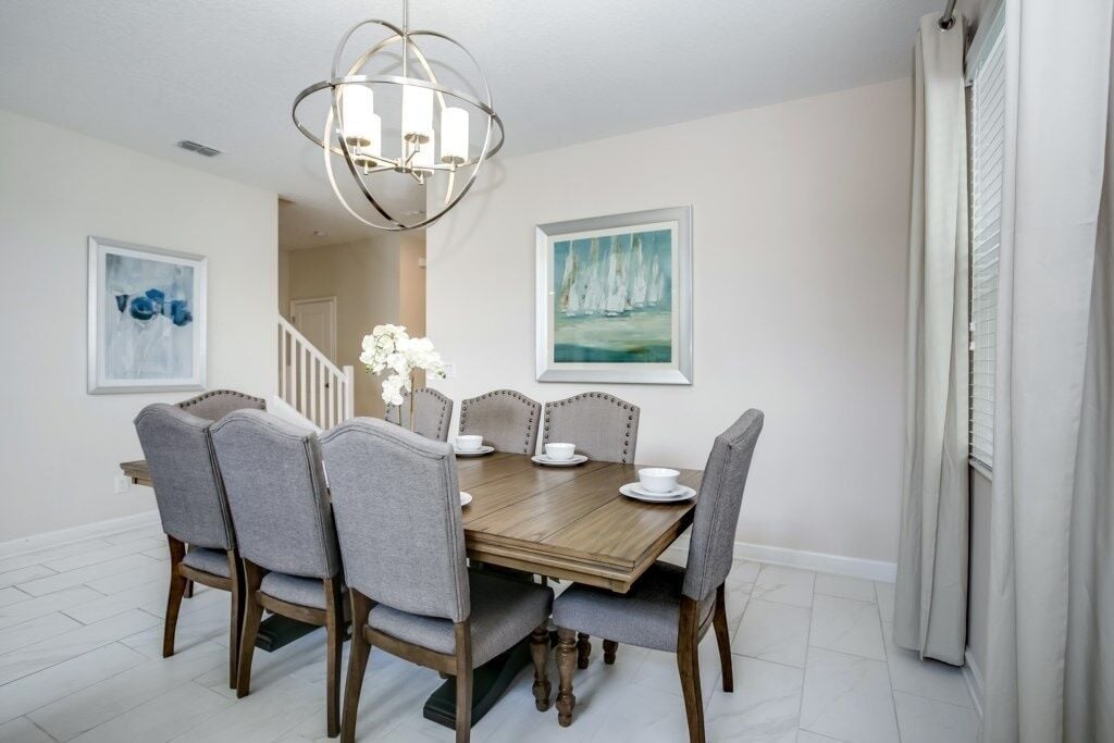 A dining room with a wooden table and six upholstered chairs, a chandelier, and two framed artworks on the walls.
