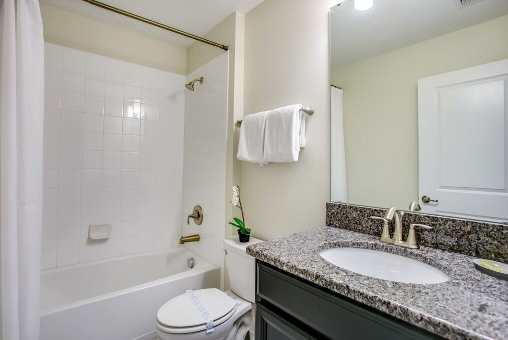 A bathroom with a white bathtub, a sink with a granite countertop, and a toilet.