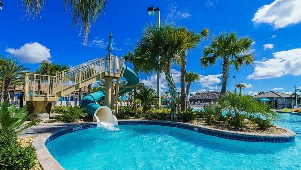 A swimming pool with a water slide, palm trees, and a clear blue sky. - 1585tempo 5 Bedroom Home by RedAwning (Davenport)
