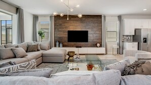 Ein modernes Wohnzimmer mit einem Ecksofa, einem Glastisch und einem Flachbildfernseher, der an einer Holzwand angebracht ist.