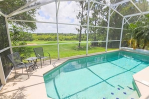 Un espace piscine avec vue sur un terrain de golf, protégé par une structure en verre.