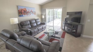 A living room with a sofa, a coffee table, a TV, and a painting on the wall. - Serene Private Pool In Southern Dunes! 4 Bedroom Home by RedAwning (Haines City)