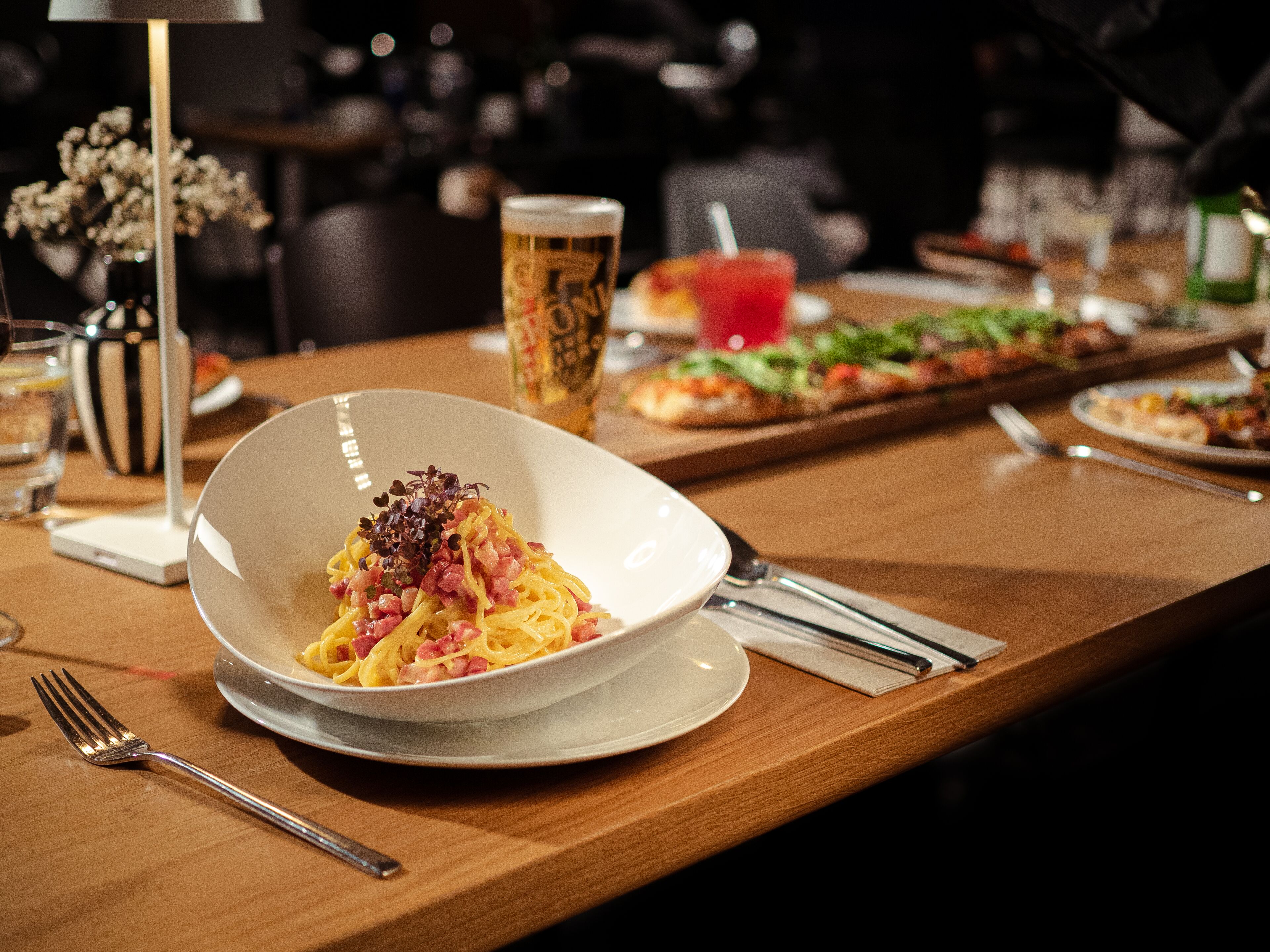 Une table à manger avec un bol de pâtes, un verre de bière et une pizza.