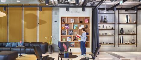 A modern interior with a black leather sofa, black chairs, a small round table, and a bookshelf with books and decorative items.