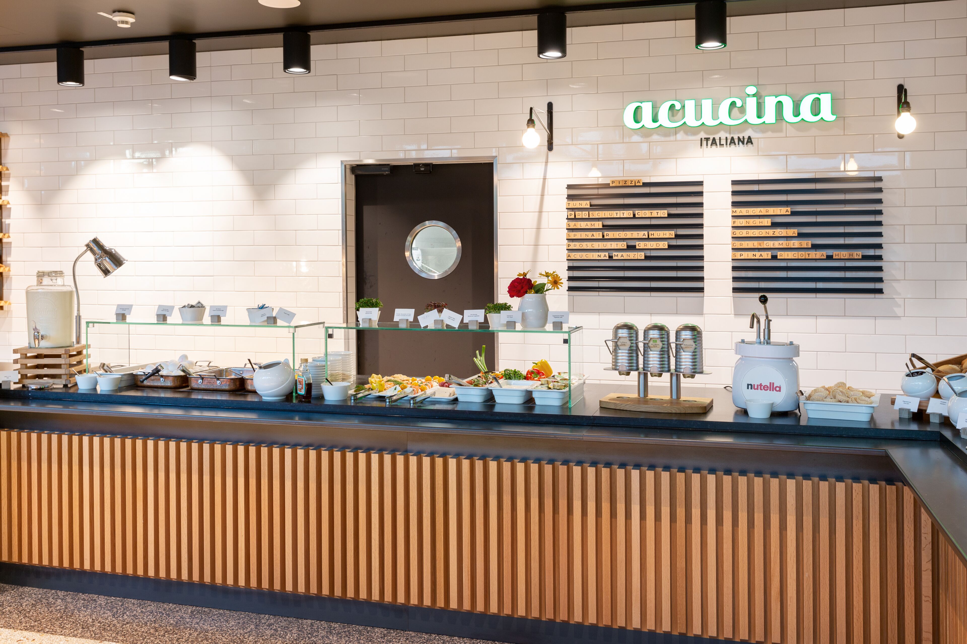 Una barra de restaurante con panel de madera, un expositor de vidrio con alimentos y un letrero que dice "acucina ITALIANA".