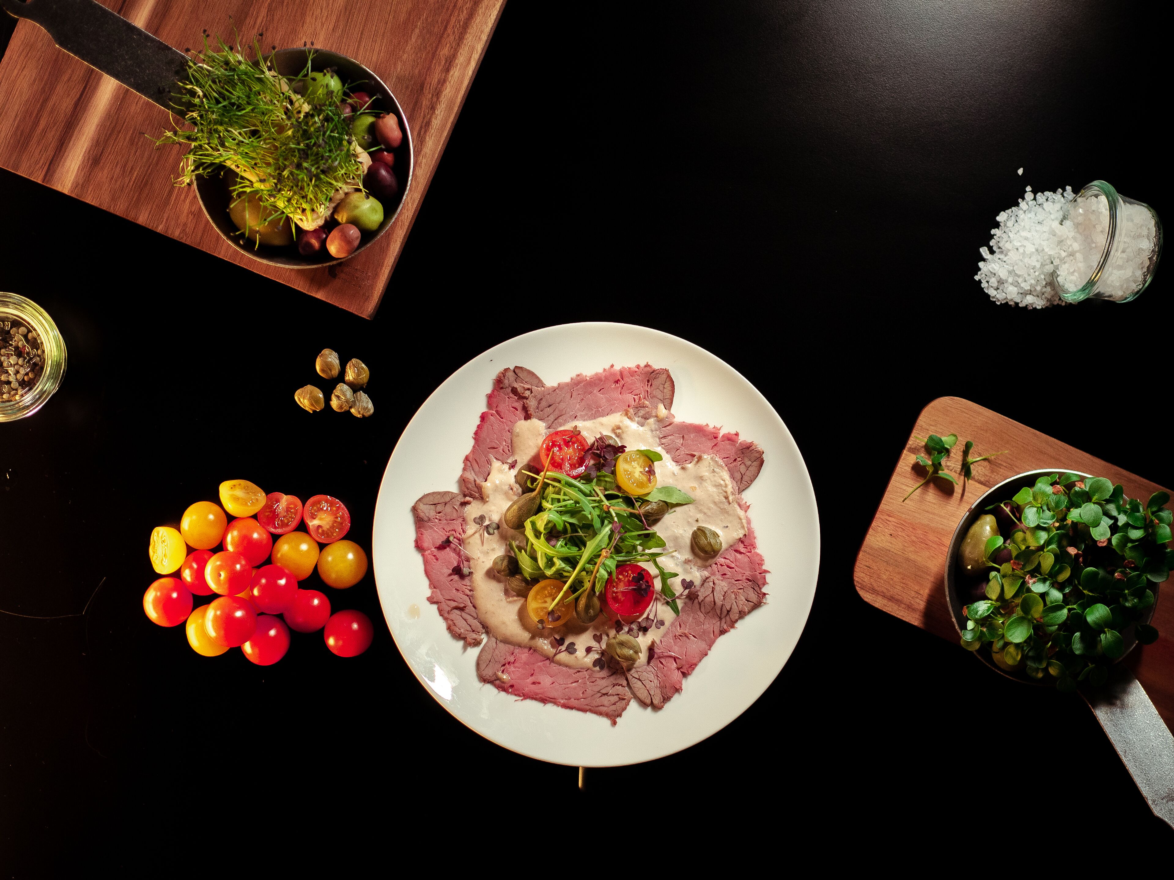 A plate of food with various garnishes and a bowl of green leaves on a wooden table.