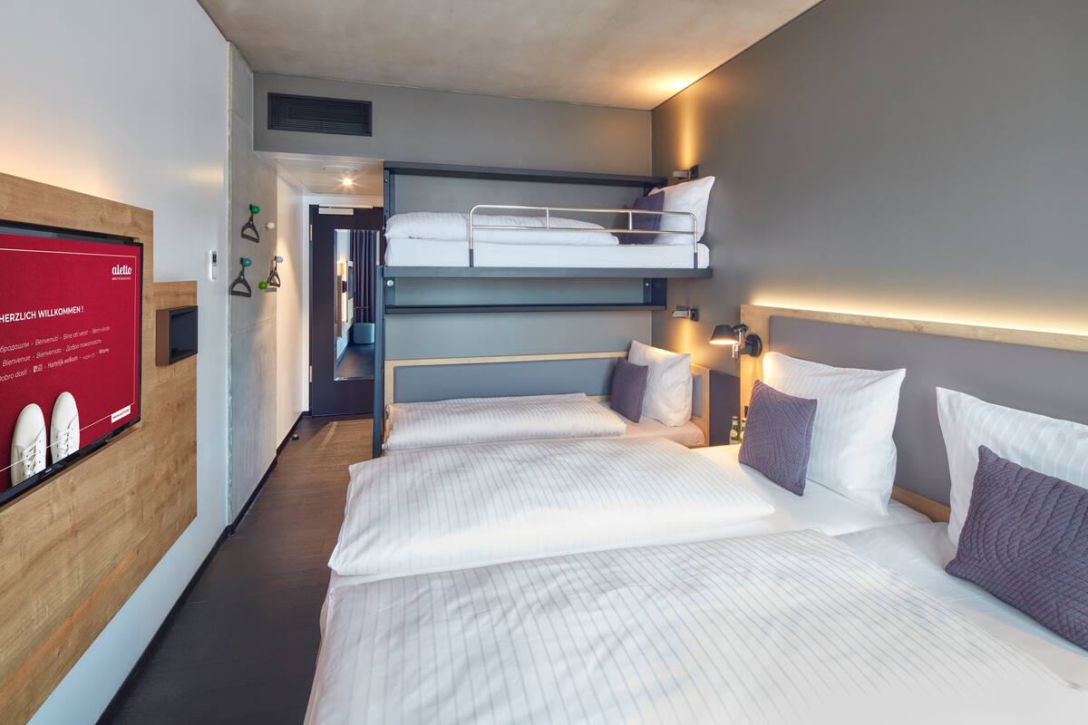 Una habitación de hotel con literas, un escritorio y un televisor instalado en la pared.