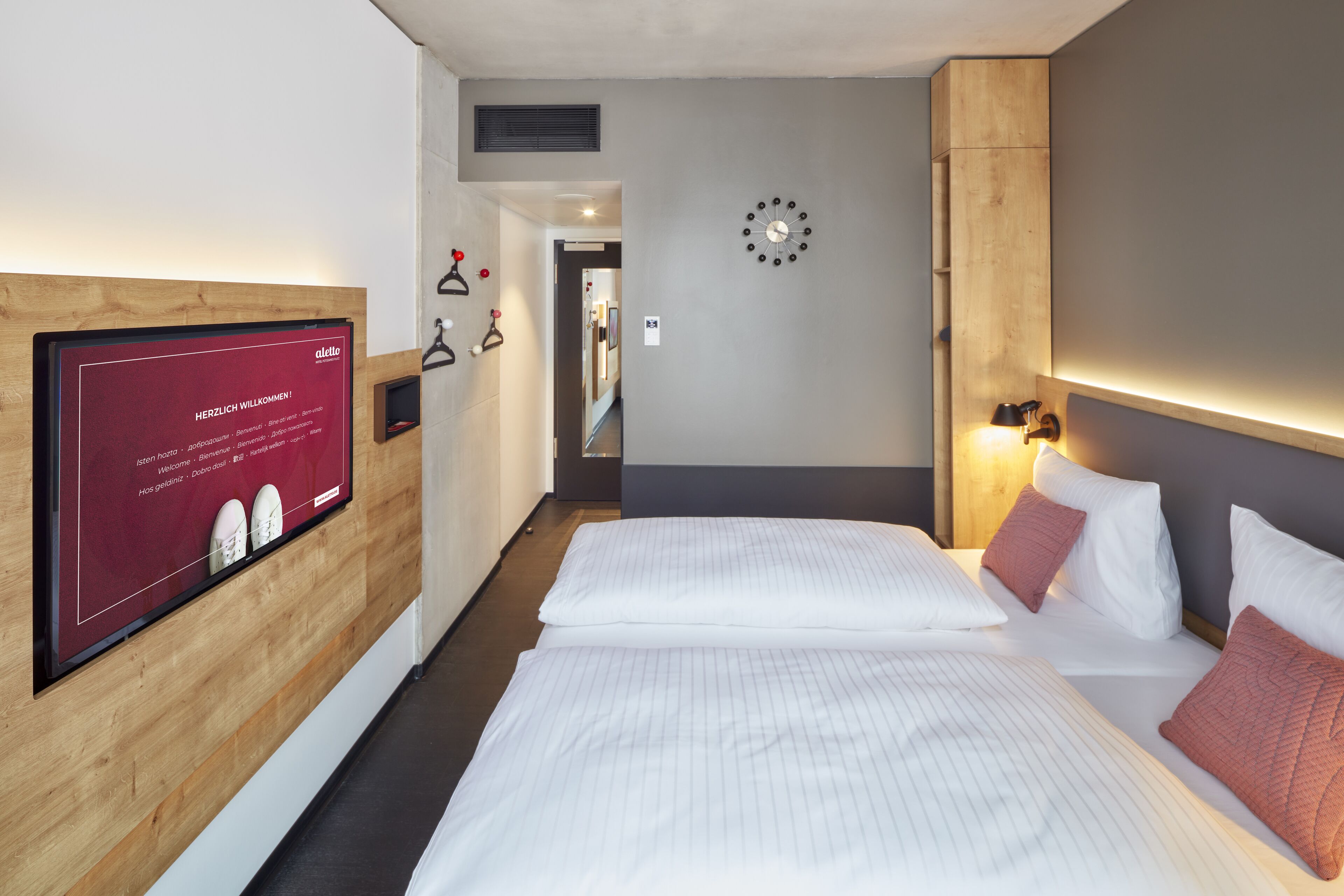 A hotel room with two beds, a wooden accent wall, a clock, and a welcome sign.